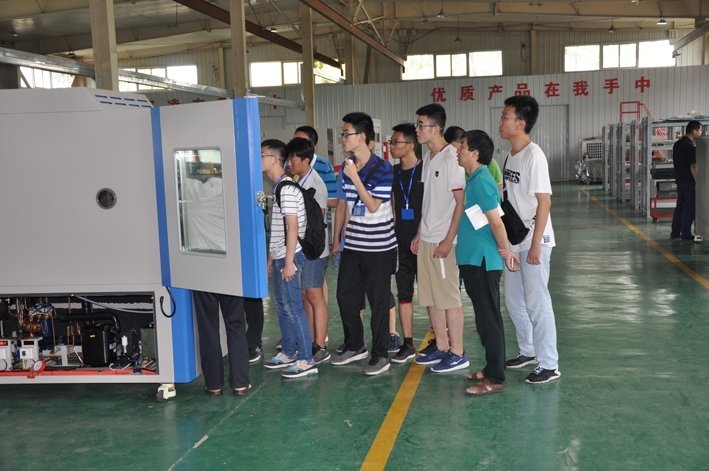 Students visiting a factory workshop and observing an environmental testing equipment unit.
